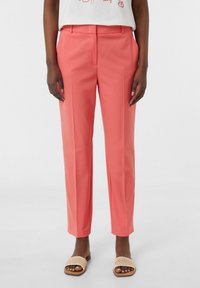Koraal kleurige taillepantalons met een rechte pasvorm, platte voorkant en twee zijzakken. Gecombineerd met lichtbruine geweven instapsandalen.