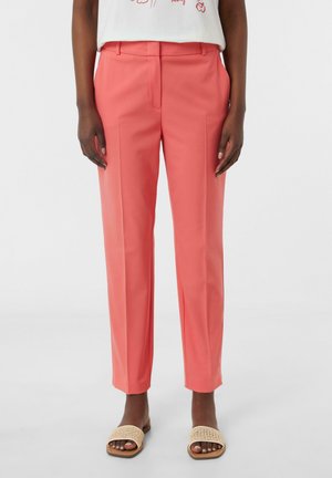 Koraal kleurige taillepantalons met een rechte pasvorm, platte voorkant en twee zijzakken. Gecombineerd met lichtbruine geweven instapsandalen.