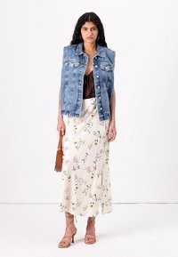 Jeansslös väst, medelblå med frambutiker. Brun topp, blommig midiklänning och lätta bruna sandaler med remmar. Enkel handväska som accent.