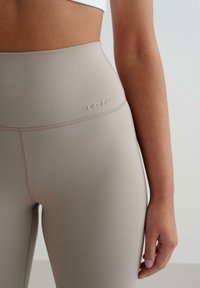 Höga ljusbeige leggings med en slät textur, med subtil sömnad och en liten logotyp från märket på midjebandet.