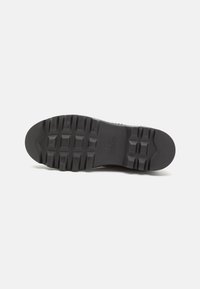 Suola di scarpa in gomma nera con un modello di grip testurizzato, caratterizzato da forme rettangolari e esagonali per la trazione e la durata.