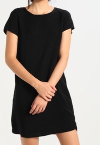 Robe noire à manches courtes avec un col rond, coupe décontractée et texture lisse, se terminant au-dessus du genou. Design simple et polyvalent.