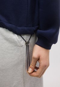 Tumesinine dressipluus soonikkoes mansettidega, millel on nööriga ümmargune hõbedane lüliti, kantud helehallide dressipükste peal.