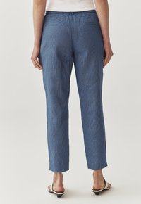Pantalones azulados con textura y diseño de pierna recta. Cuentan con bolsillos traseros y una cinturilla suave. Combinados con sandalias blancas.