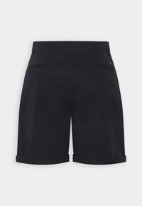 Short noir sur mesure avec ourlets retournés et deux poches passepoilées à l'arrière sur un fond clair uni.