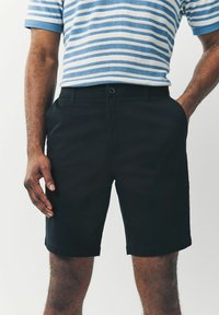 Pantalones cortos negros con una textura suave, que cuentan con un cierre de botón, bolsillos laterales y un diseño de corte recto. Aptos para uso casual.