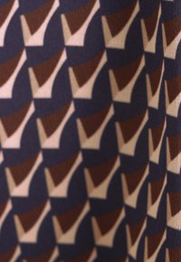 Tissu avec un motif géométrique de formes brunes et crème sur un fond bleu foncé, comportant des zones lisses et texturées en alternance.