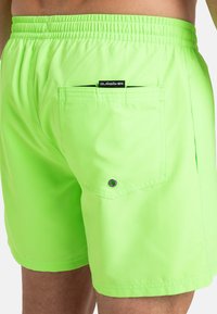 Shorts de baño verde neón con cintura elástica, un bolsillo trasero y etiqueta del logo de Quiksilver cosida encima del bolsillo.