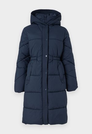 Sötétkék puffermellény, kapucnival, bordázott gallérral, elöl patentos záródással és két oldalsó zsebből áll, amelyeket steppelt textúra és párnázás jellemez.