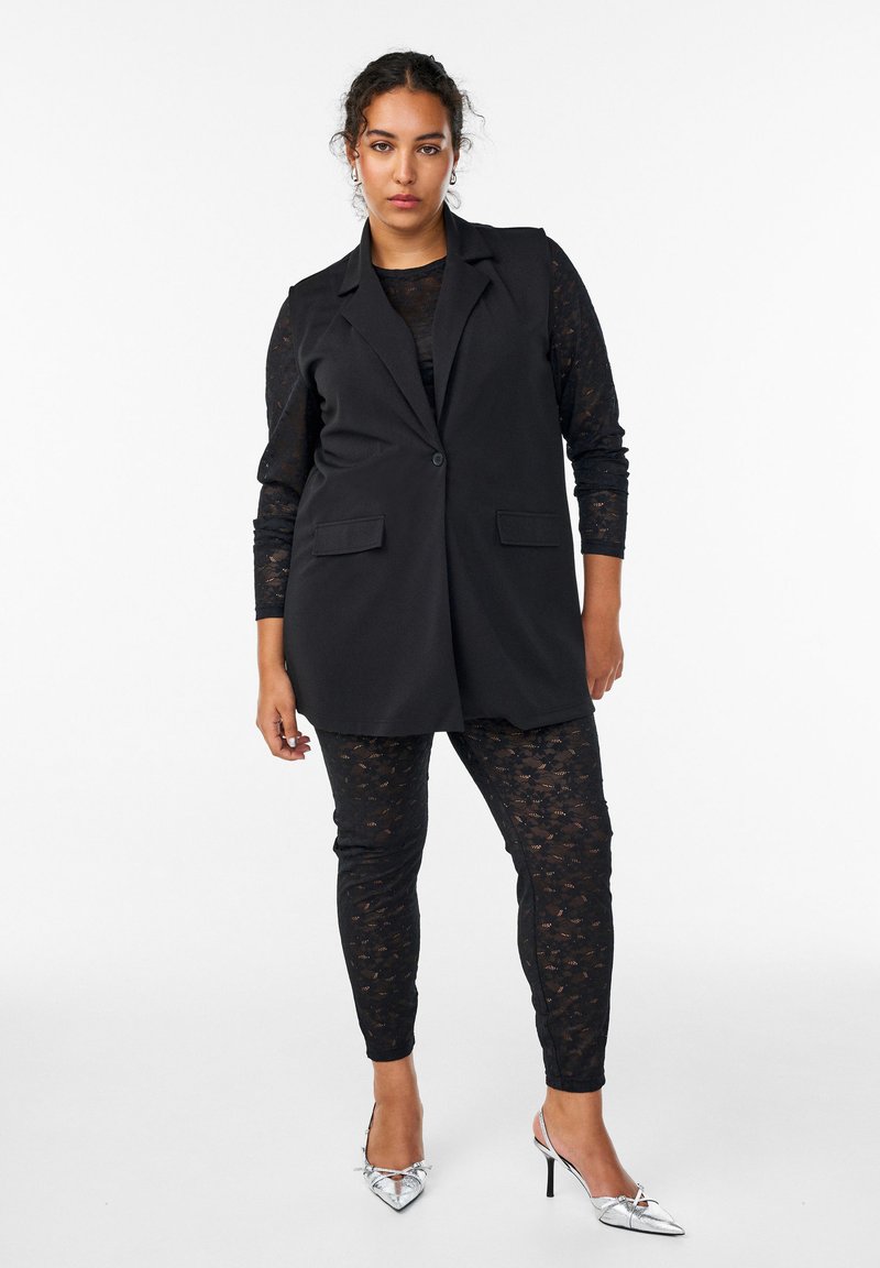 Musthave mustreid blazer ilma varrukat, laitsega, kahe eesmine taskutega, kombineeritud musta pitsilise pikkade varrukatega toppiga ja mustade mustritega pükstega. Hõbedased kõrged kontsad.
