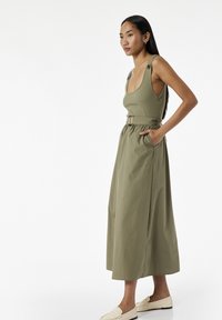 Oliven grøn maxi kjole med justerbare stropper, samlede talje og sidelommer. Kompletteret med lysebeige slip-on sko.