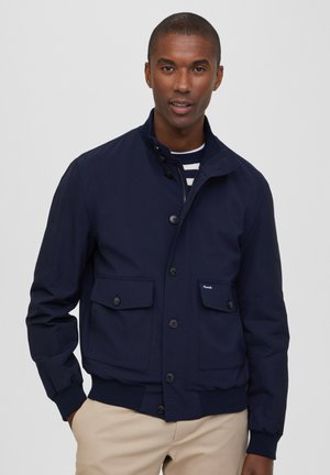 Chaqueta azul marino con cuello alto, cierre de botones y dos bolsillos frontales. Presenta puños acanalados y una tela texturizada.