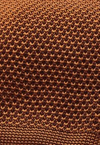 Bruin gebreid stof met een gestructureerd patroon, met verschillende tinten oranje en bruin, strak geweven voor duurzaamheid.