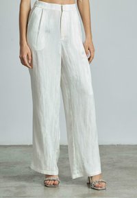 Pantalons larges à taille haute en tissu blanc texturé et brillant. Comprend des plis sur le devant et une fermeture éclair. Assortis à des talons embellis.