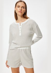 Stribet loungewear sæt med en langærmet top med knapper og rund halsudskæring, parret med shorts med elastik i taljen, i lyse farver.