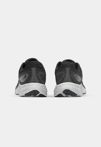 Baskets noires de sport avec une tige en mesh texturé, un col rembourré et une semelle intermédiaire blanche avec des semelles en caoutchouc noir. Présente un logo sur le côté.