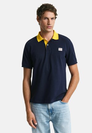 Navy polo shirt met een gele kraag; korte mouwen, zacht katoenmateriaal, voorzien van een klein logo op de borst.