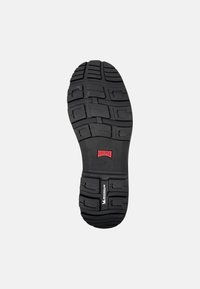 Suela de zapato de goma negra con patrones de dibujo profundos, que presenta un prominente logo rojo, superficie texturizada y bordes reforzados para mayor durabilidad.