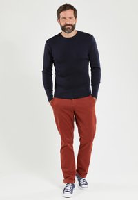 Marine gebreide trui, rode broek, blauwe sneakers. De trui heeft schouderknopen; de broek heeft een gladde textuur, beide zijn aangesloten voor een op maat gemaakte uitstraling.