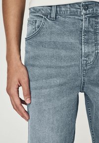 Jeans din denim de culoare bleu deschis cu un finisaj ușor uzat. Prezintă cinci buzunare, închidere cu nasture și un design cu picior drept. Textură netedă.