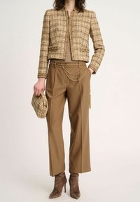 Béžový tweedový kabát se zlatými akcenty, béžový top, široké hnědé kalhoty, ladící psaníčko a hnědé kotníkové boty s tenkým podpatkem.