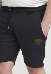 Black cotton shorts with side pockets, adjustable drawstring waistband, and a gold graphic logo featuring the phrase "CREATE TOMORROW."