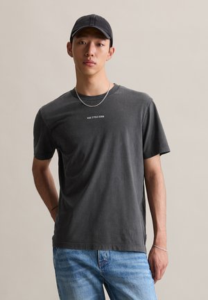 Gray cotton t-shirt with short sleeves and a crew neckline, featuring white text in the center. Paired with light blue denim jeans.