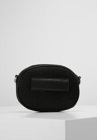 Zwarte ovale tas gemaakt van gaasmateriaal met een gladleren accent. Heeft een platte schouderband en metalen hardware. Textuur voor extra grip.