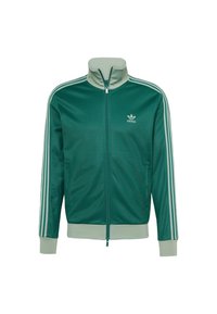 Grön zip-up jacka i slätt tyg med hög krage, med tre vita ränder på varje ärm och en liten vit logga på bröstet.