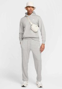 Haut de survêtement gris avec une poche frontale et un cordon de serrage, survêtement assorti, baskets blanches et un petit sac léger porté à l'épaule. Chapeau à large bord.