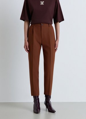 Persona che indossa pantaloni marroni a vita alta, stivali bordeaux scuro e una camicia marrone scuro con il testo "CALM AND COOL".