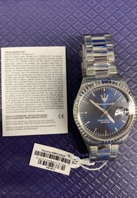 Silver metal wristwatch with a blue dial, date feature, and a stainless steel bracelet. Includes a warranty tag and instruction manual.