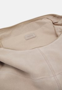 Beiges Wildleder-Tascheninnere mit glatter Textur, Reißverschlussverschluss und einem rechteckigen Etikett, das mit "ANNA FIELD" geprägt ist. Keine sichtbaren Fächer.