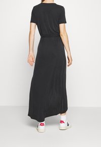 Musta, lyhythihainen maksimekko, jossa on nauhavyötärö, valmistettu sileästä ja kevyestä kankaasta, ja yhdistettynä rentoihin valkoisiin tennareihin.