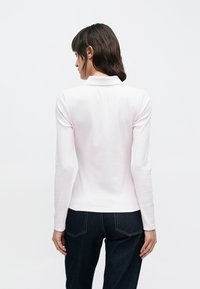 Polo a maniche lunghe di colore rosa chiaro con collo, trama a costine e design aderente, abbinata a pantaloni in denim scuro.