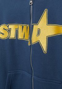 Navy blue zip-up hoodie with large yellow embroidered text partially reading "STWA" and a prominent yellow star on the chest area.