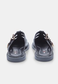 Black sandals with a shiny patent finish, open back design, and gold-tone hardware accents. Flat sole with textured detail.