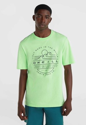 Camiseta de algodón verde claro con un gráfico circular que incluye texto y un diseño de olas. Mangas cortas, cuello redondo, ajuste relajado.