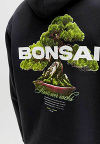 Schwarzer Hoodie mit detailliertem Bonsai-Baum-Grafik, großem "BONSAI"-Schriftzug und dem kleineren Schriftzug "Roots over rocks" auf der Rückseite.