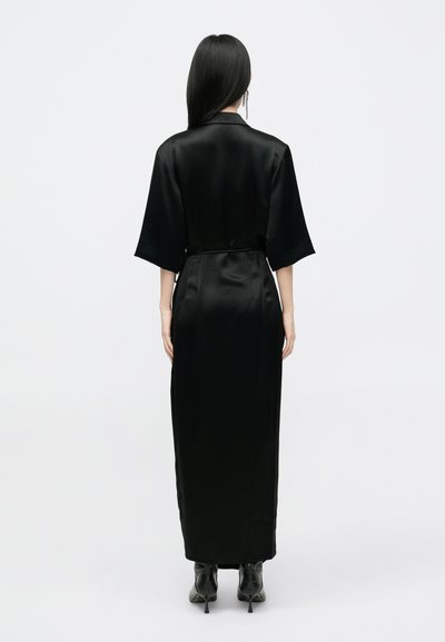 Vestido de cetim preto com um corte longo e reto, mangas curtas estilo quimono e faixa na cintura. Textura suave, design minimalista e comprimento até o tornozelo.