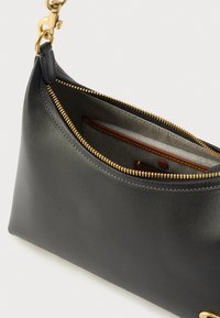 Μαύρη δερμάτινη τσάντα χειρός με καμπυλωτό σχήμα, χρυστό φερμουάρ και ορειχάλκινα εξαρτήματα. Το εσωτερικό περιλαμβάνει καφέ δερμάτινη θήκη σε ριγέ φόδρα.