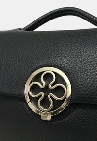 Sac en cuir noir texturé avec un fermoir circulaire doré arborant un motif floral à quatre boucles sur le rabat avant.