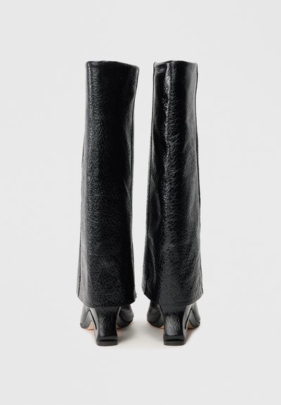 Čierne kožené čižmy s lesklou textúrou, vysokou skaľou, blokovými opätkami a jedinečným uhlovým dizajnom. Čisté línie, bez viditeľných ozdôb.