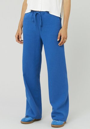 Pantalons larges bleus en tissu texturé, avec une taille à cordon de serrage et des poches latérales, associés à des chaussures bleues à enfiler.