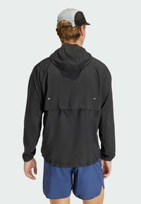 Μαύρο ελαφρύ μπουφάν με κουκούλα, που διαθέτει αντιθετικό πίσω πάνελ και μινιμαλιστικό σχέδιο. Υφασμάτινη υφή με ανακλαστικές λεπτομέρειες.