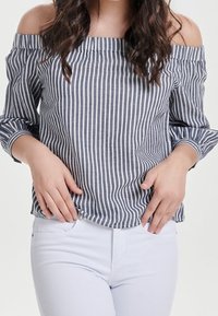 Striped off-shoulder top in navy and white. Features a relaxed fit, long sleeves, and a straight hem. Paired with white jeans.