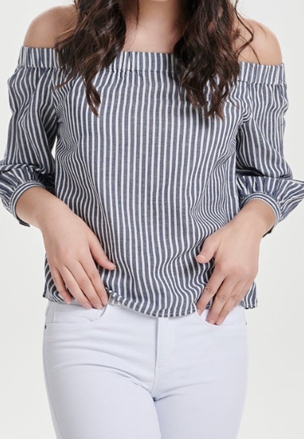 Striped off-shoulder top in navy and white. Features a relaxed fit, long sleeves, and a straight hem. Paired with white jeans.
