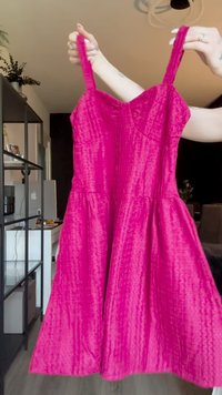 Helles rosa Kleid mit tailliertem Oberteil, dünnen Trägern und weit schwingendem Rock. Strukturierter Stoff mit vertikalen Linien und sanftem Glanz.