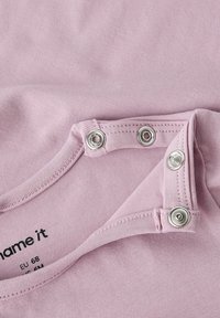 Lichtroze katoenen stof met drukknoopsluitingen langs de hals. Heeft een zachte textuur en subtiele rek, geschikt voor baby's tot 6 maanden.