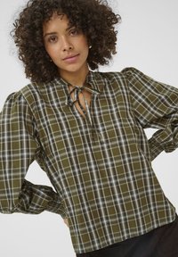 Chemise à carreaux verts avec un col cravate, de longues manches bouffantes et des poignets froncés. Fabriquée en tissu léger à motif à carreaux.